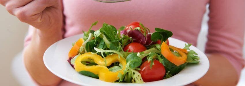 woman holding large bowl of salad tomatoes and yellow and orange peppers