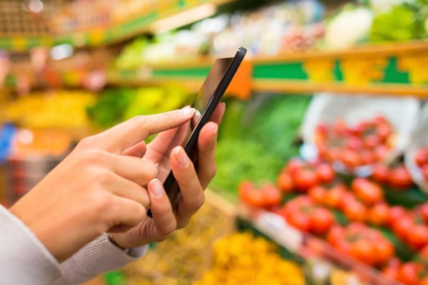 woman on phone at grocery store reading brick bodies padonia blog for meal prep