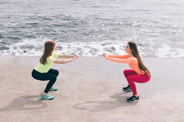 women taking brick bodies gyms tips and squatting while vacationing at beach