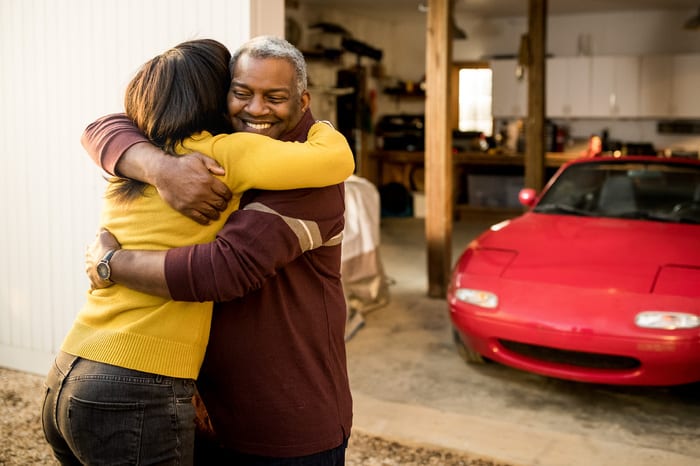 man and woman embracing outdoors in front of red car inside of garage