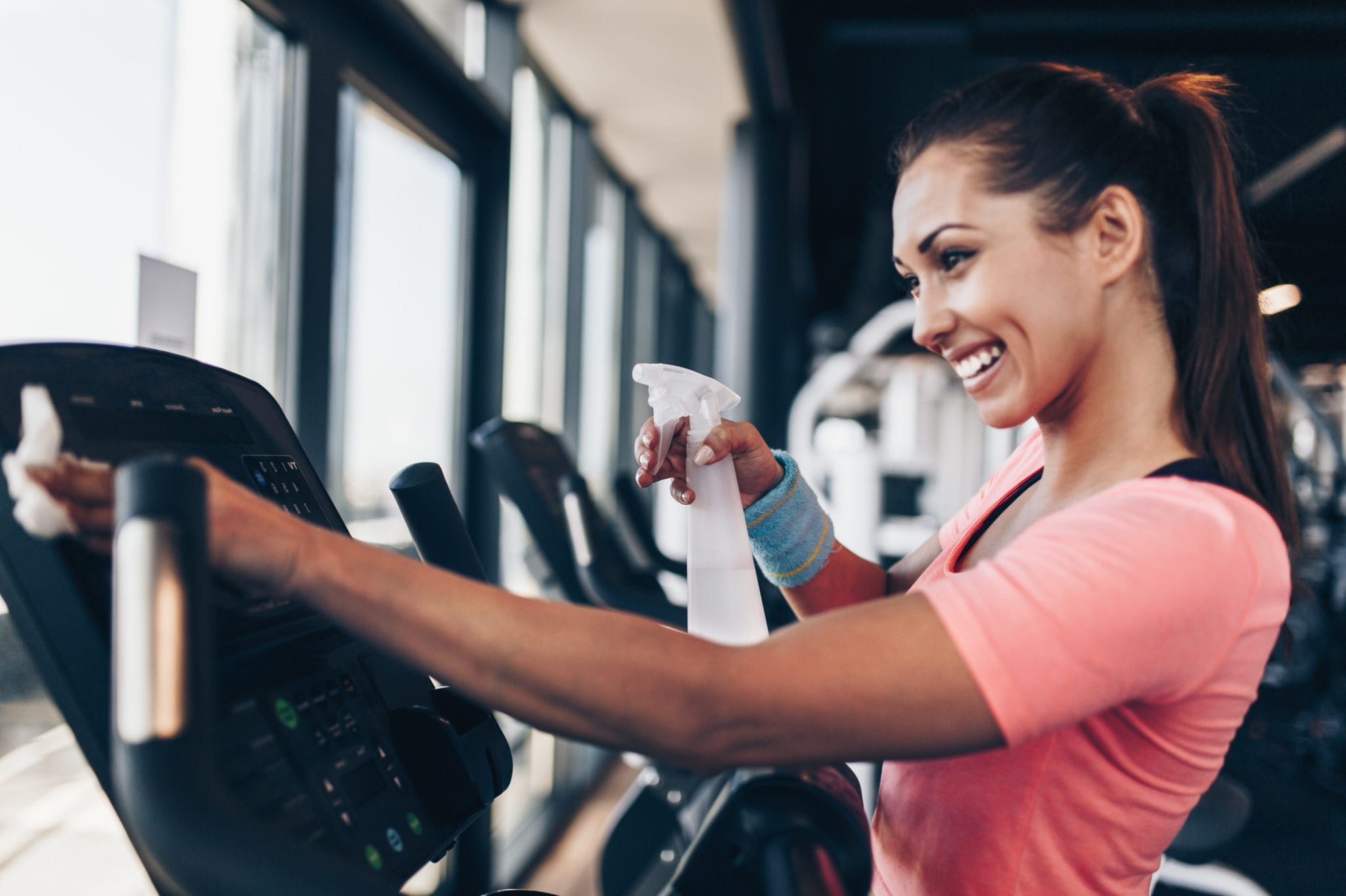 gym member using disinfectant spray and paper towel to wipe down cardio training equipment