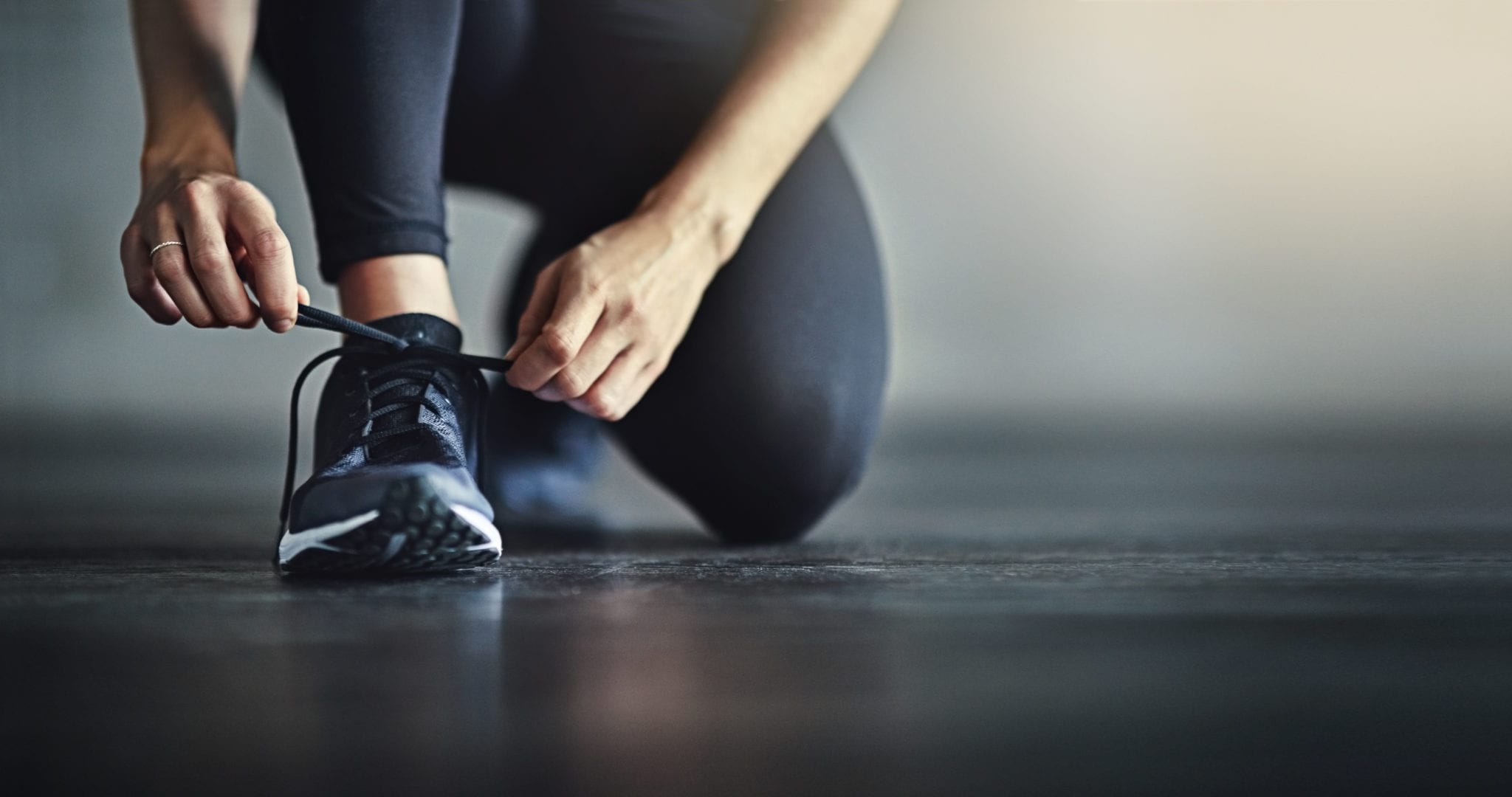 woman in fitness apparel lacing up shoe for cardio training workout at brick bodies gym