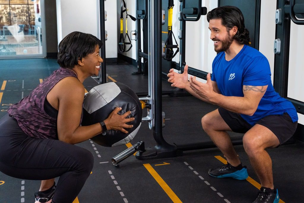 Personal trainer and woman squatting with slamball